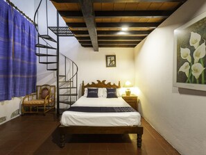 Ein Schlafzimmer mit einem hölzernen Bett, einer Wendeltreppe, einem Sessel, einem Nachttisch und einem Wandbild.