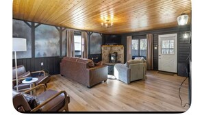 A cozy cabin interior with a wooden ceiling, a stone fireplace, leather sofas, and a television. - sleeps six, close to slopes, hot tub and game room private hot tub (Albrightsville)