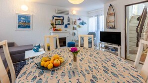 Un coin repas avec une table ronde, des chaises, un vase de fleurs et un saladier de fruits.