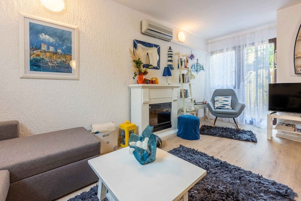 A living room with a sofa, a table with a decorative vase, a fireplace, a TV, and a bookshelf.