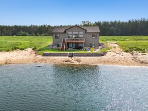 A two-story house with a deck, a swimming pool, and a grassy landscape.
