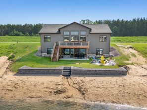 Une maison à deux étages dotée d’un balcon, d’une terrasse et d’un espace aménagé avec un foyer extérieur.