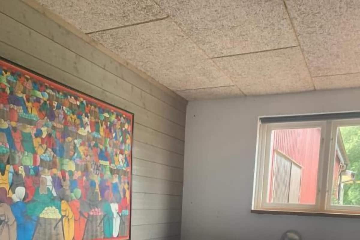 Ein Schlafzimmer mit einem hölzernen Bett, einem farbenfrohen abstrakten Gemälde an der Wand und einem Fenster mit Blick auf ein rotes Gebäude.