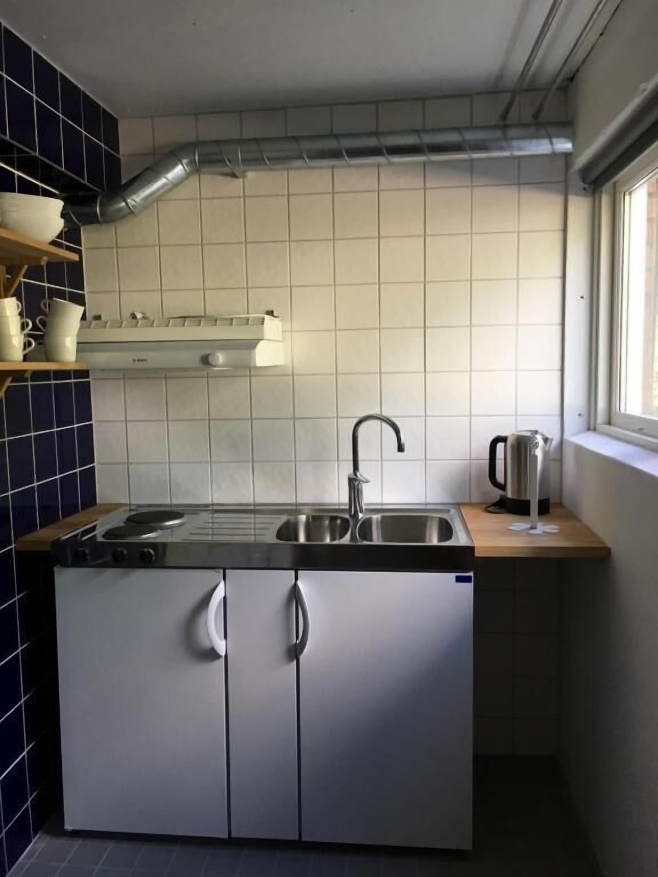 Una cocina compacta con lavabo, estufa y alacenas, una ventana y una cafetera sobre la encimera.