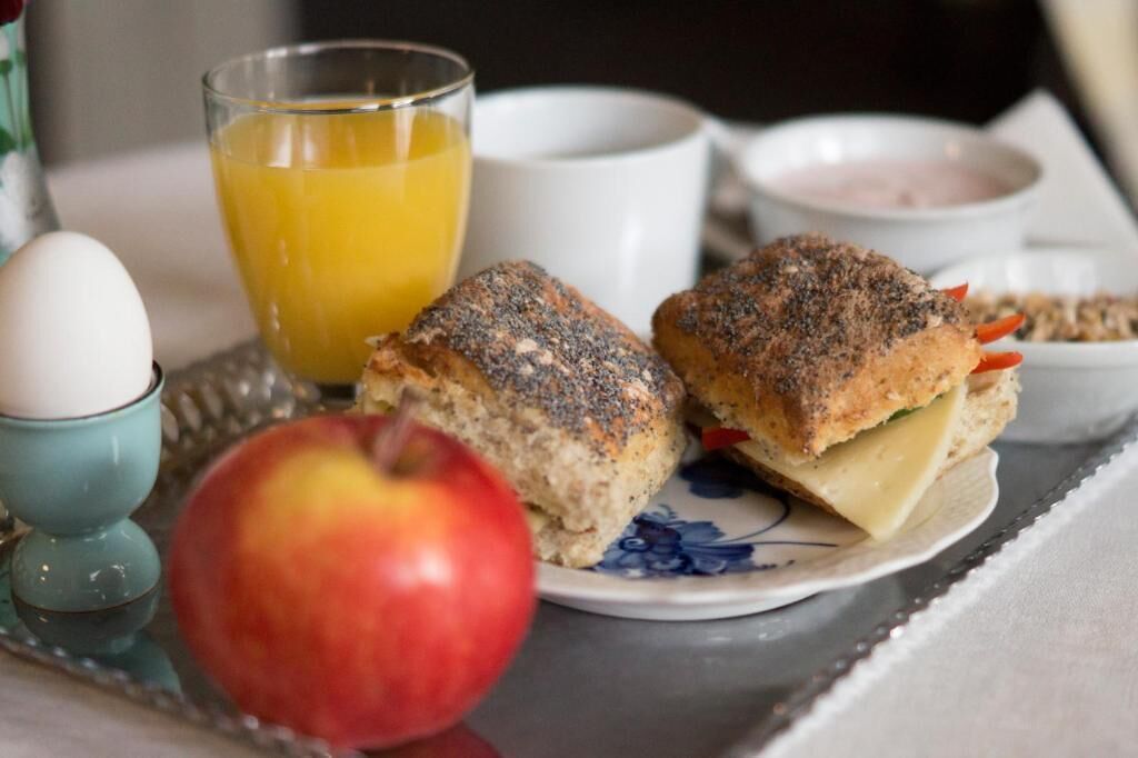 Un plat petitdejuni amb dos entrepans, una poma, un got de suc d'aranja i una tassa de cafè.