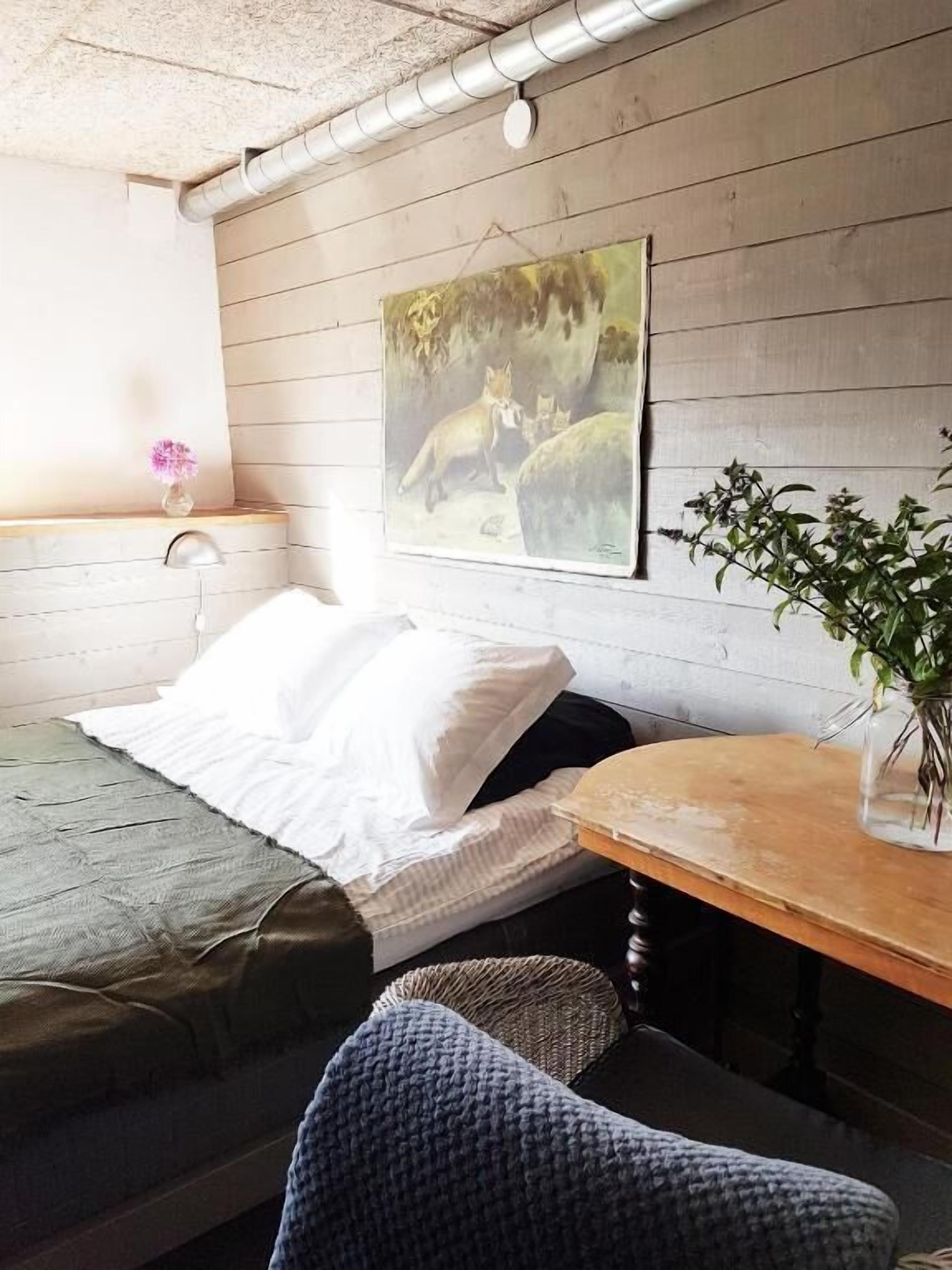 Una habitación con cama, una mesita, una silla, un cuadro de zorros y una planta en maceta.