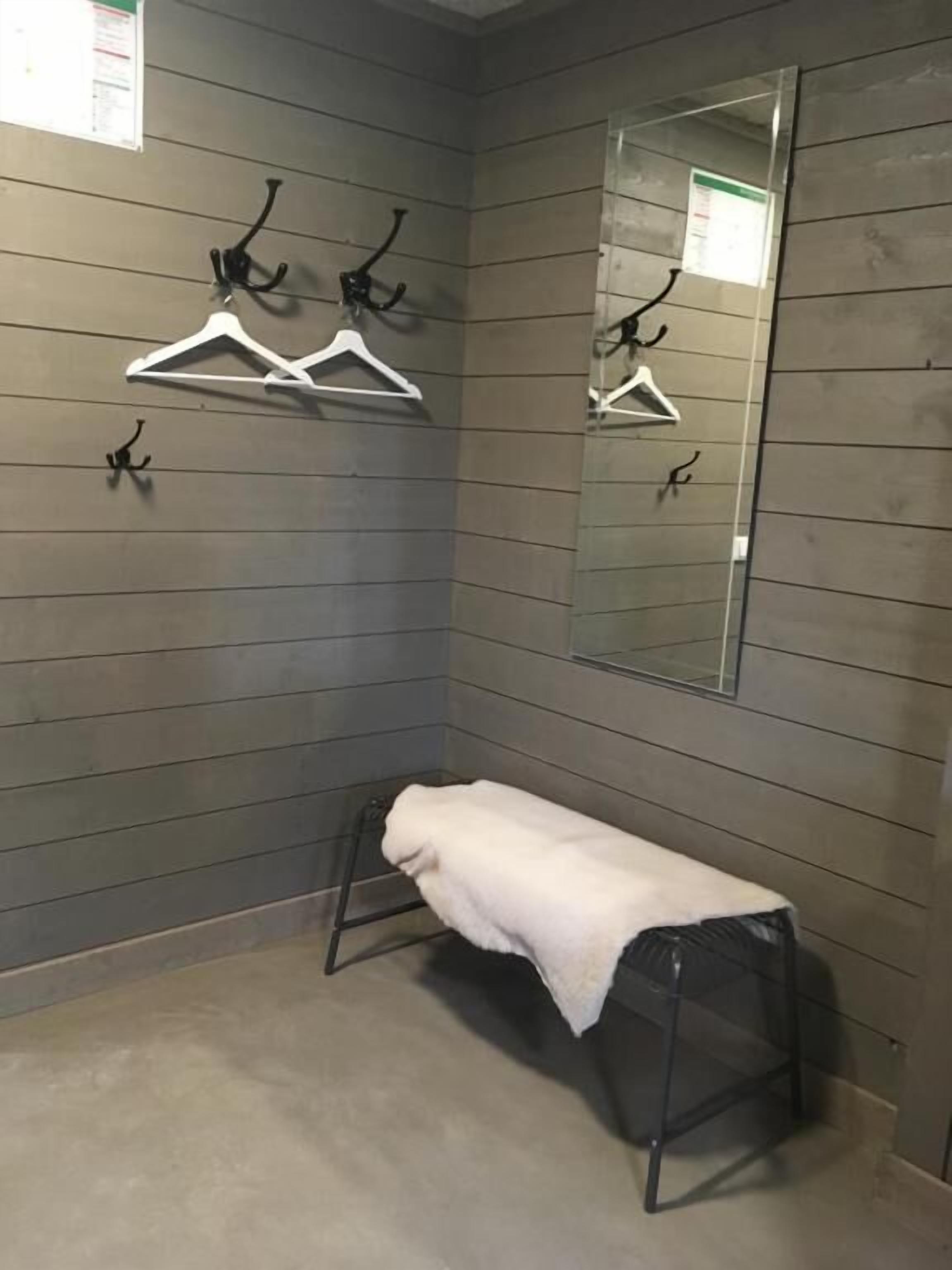 A corner of a room with grey walls, a bench with a white towel, and a mirror on the wall.