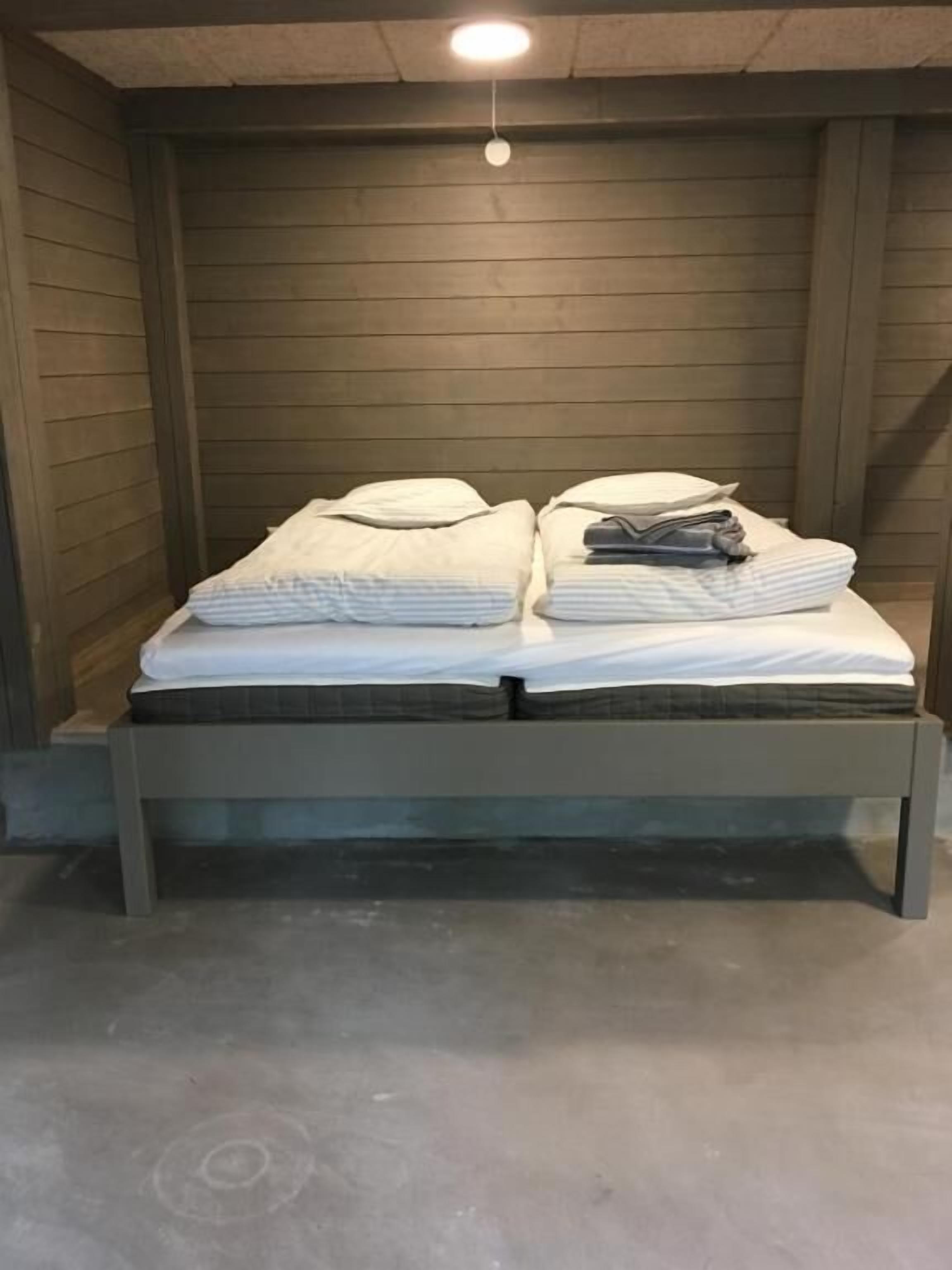Une petite pièce comprenant un lit, une petite table et un luminaire au plafond.