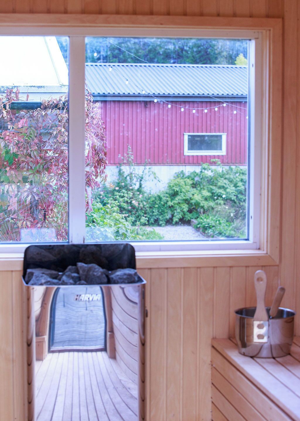A wooden cabin with a window overlooking a red barn and greenery.