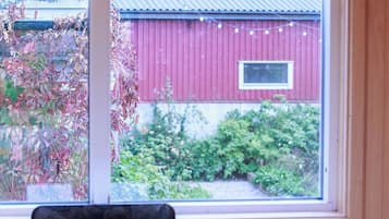 A wooden cabin with a window overlooking a red barn and greenery.