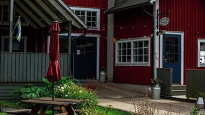 Un bâtiment rouge avec une porte et des fenêtres bleues, un patio couvert avec un parasol rouge et une table de pique-nique.