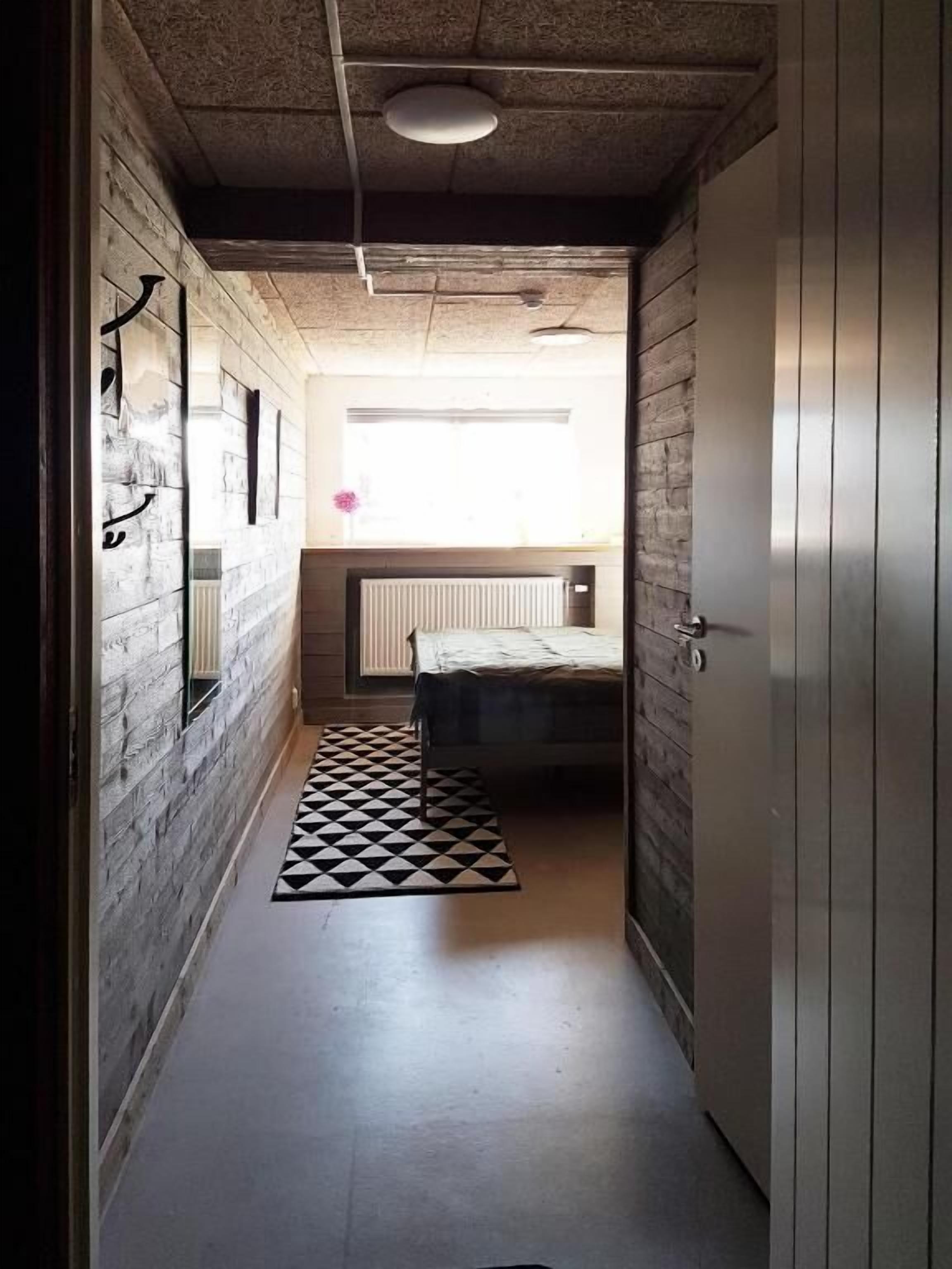 A narrow hallway with a bed at the end, a radiator, and a patterned rug.
