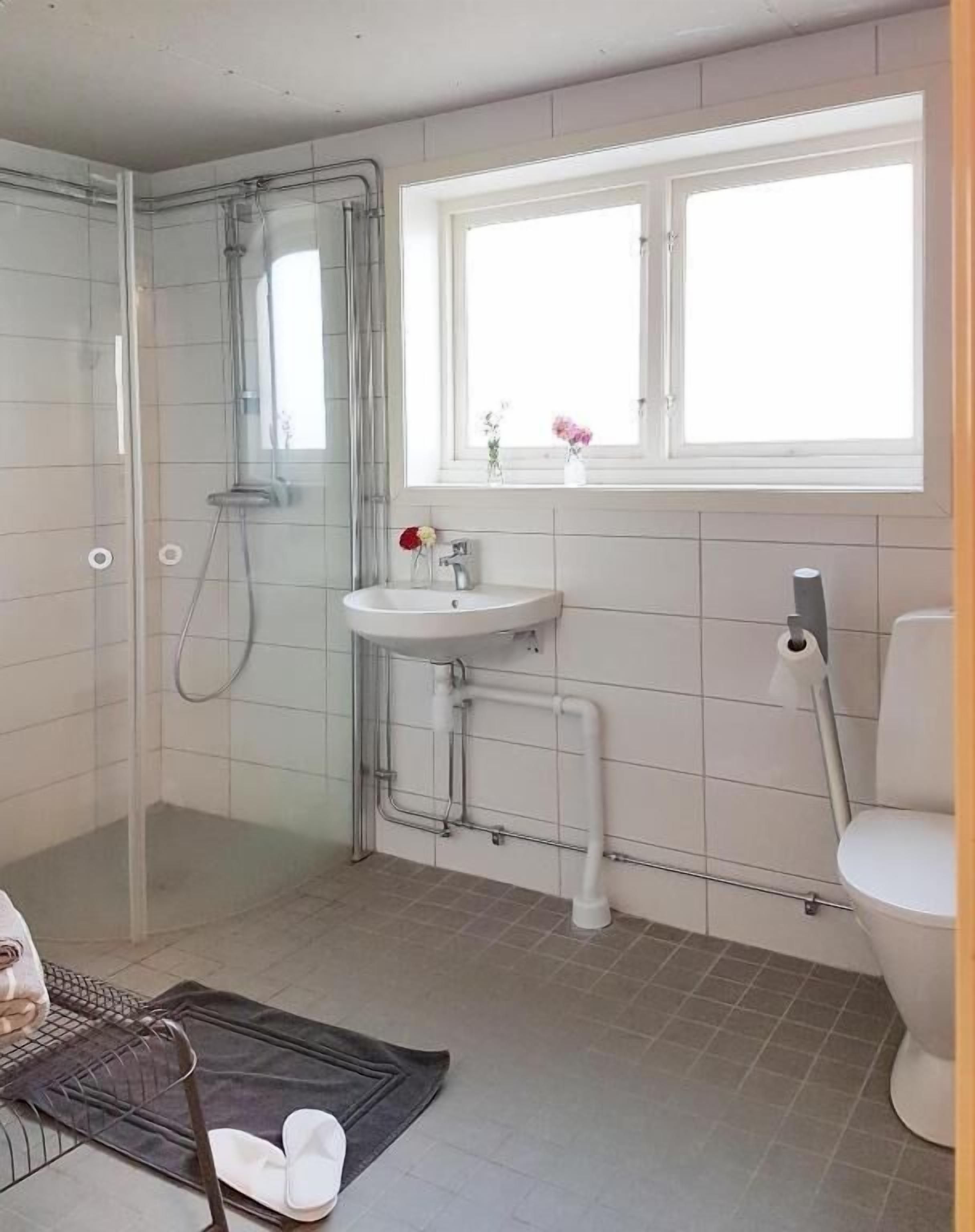 Een badkamer met een douchecabine van glas, een wastafel, een toilet en een raam met bloemen.