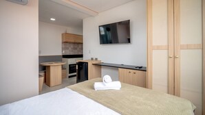 Una moderna camera d'albergo con un letto, una TV fissata al muro, un angolo cottura e un armadio in legno.