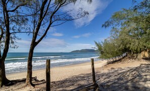 Ein Strand mit einer Holzzaun, Bäumen und Blick aufs Meer.