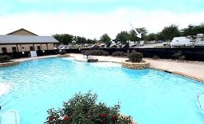 Ein Schwimmbecken mit Steinbord, eine kleine Gartenanlage mit roten Blumen und ein Gebäude mit geneigtem Dach im Hintergrund.