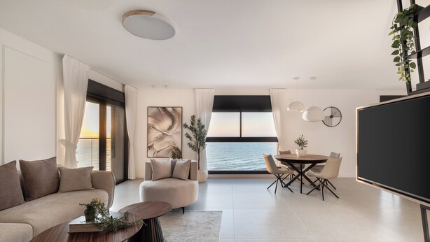 A modern living room with a sofa, coffee table, and dining area. There is a large window with a view of the ocean.