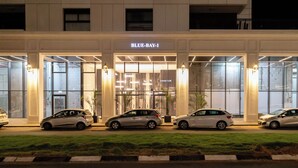 A modern building with the sign "BLUE-BAY-1" at the entrance. There are three cars parked in front.