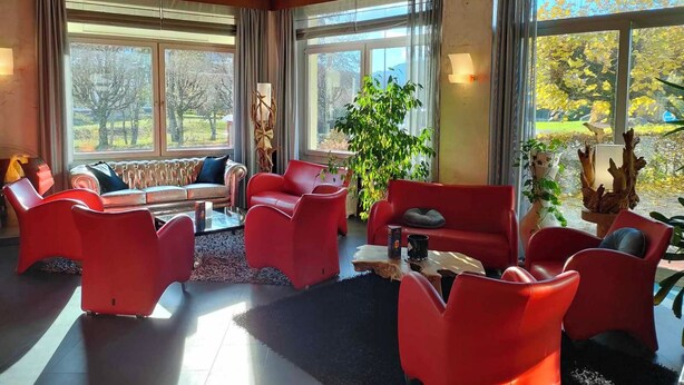 A spacious room with large windows, a red sofa, red chairs, and a coffee table. - Lannexe By La Réserve (Gerardmer)