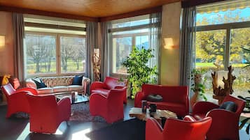Ein geräumiger Raum mit großen Fenstern, einem roten Sofa, roten Sesseln und einem Couchtisch.