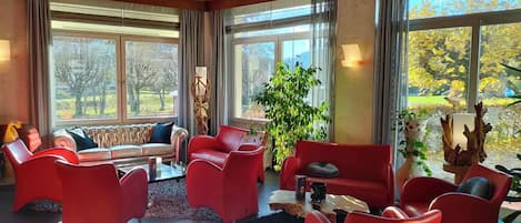 Una habitación amplia con ventanas grandes, un sofá rojo, sillas rojas y una mesa de centro.