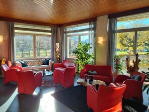 A spacious room with large windows, a red sofa, red chairs, and a coffee table. - Lannexe By La Réserve (Gerardmer)
