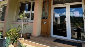 El exterior de Le P'tit Hotel du Lac, con un letrero, una puerta de madera con un adorno en forma de corazón y plantas en macetas en los escalones.