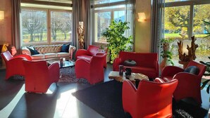 Una habitación amplia con ventanas grandes, un sofá rojo, sillas rojas y una mesa de centro.