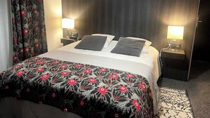 A hotel room with a bed, two bedside tables with lamps, a patterned bedspread, and a window with curtains. - Lannexe By La Réserve (Gerardmer)