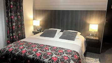 Ein Hotelzimmer mit einem Bett, zwei Nachttischen mit Lampen, einer gemusterten Bettdecke und einem Fenster mit Vorhängen.