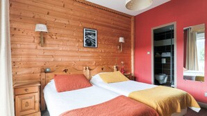A double bed with two red and one yellow blanket, wooden paneling on the walls, a framed picture, and a window with curtains. - Lannexe By La Réserve (Gerardmer)