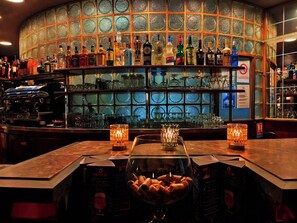 A bar with a glass display case filled with snacks, a variety of liquor bottles, and a coffee machine. - Lannexe By La Réserve (Gerardmer)