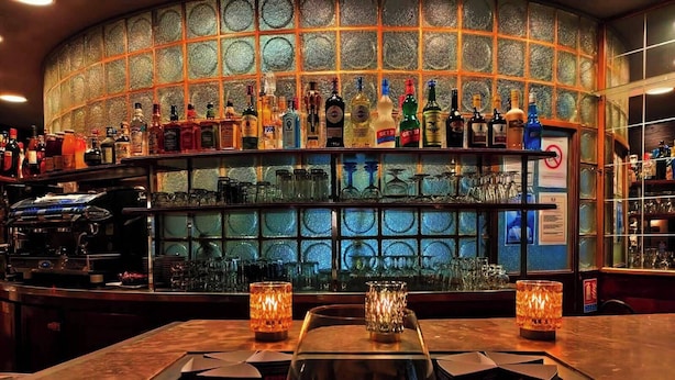 Un bar con una vitrina llena de aperitivos, una variedad de botellas de licor y una máquina de café.