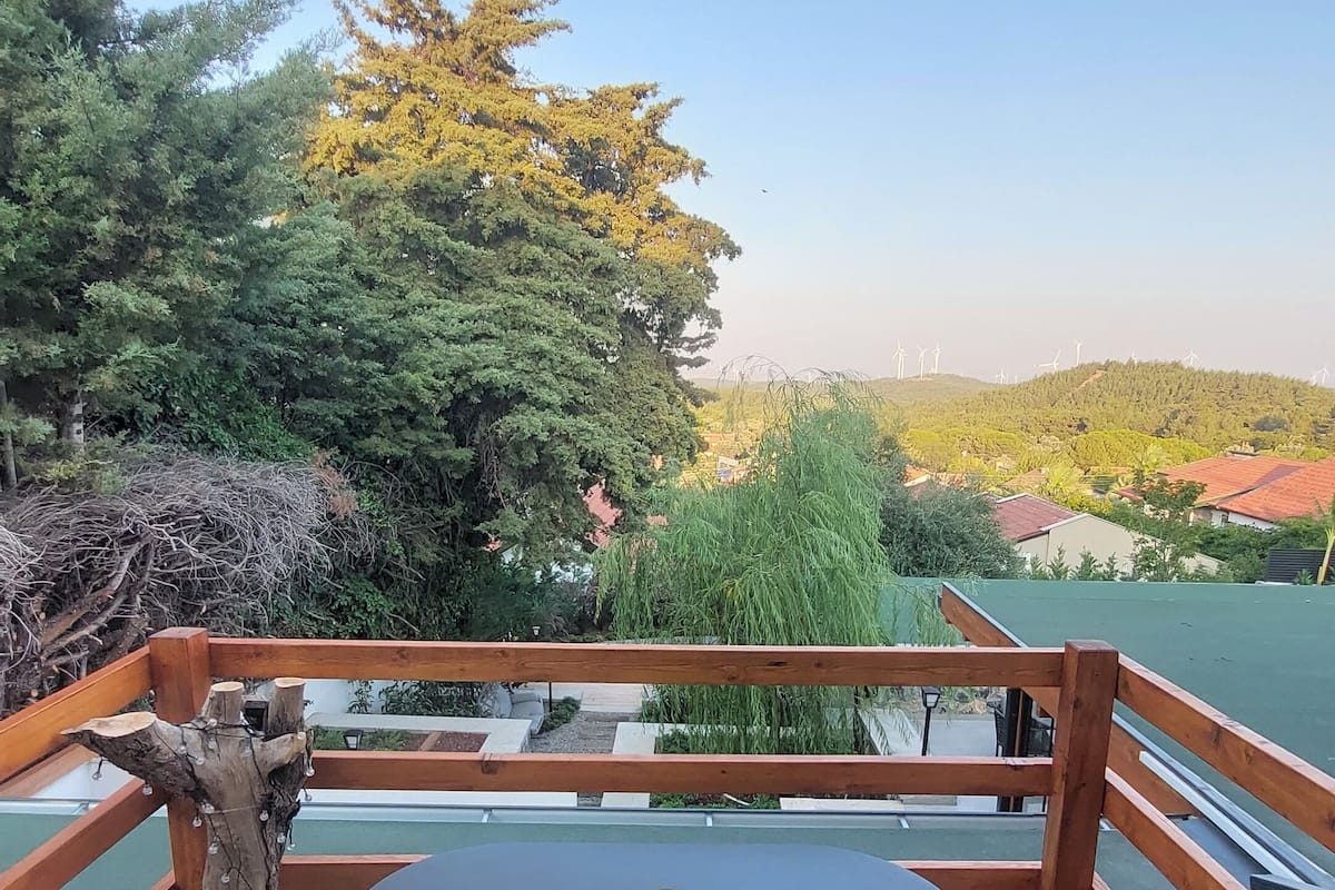 A wooden deck with wicker chairs and a table, overlooking a body of water and greenery.