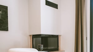 A modern living room with a white armchair, a flat-screen TV on a stand, a small table with a glass, and a window with curtains. - The Ascents of Urla (Urla)