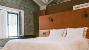 A bedroom with a stone wall, a wooden headboard, a bed with white bedding, and a window with curtains. - The Ascents of Urla (Urla)