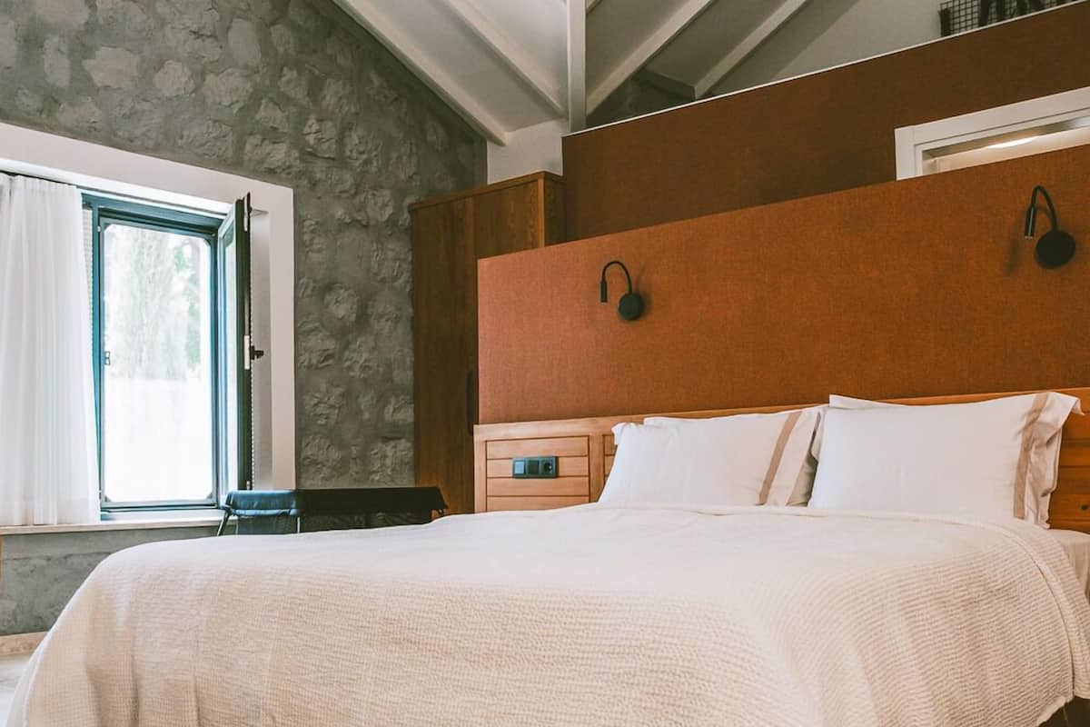 A bedroom with a stone wall, a wooden headboard, a bed with white bedding, and a window with curtains.