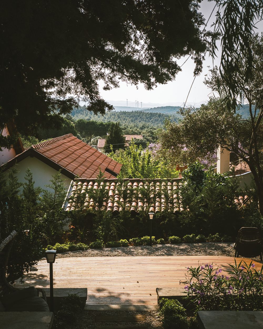 Un patio con techo de baldosas, rodeado de follaje y una terraza de madera.