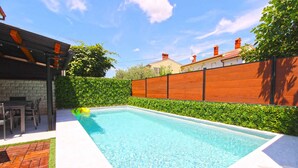 A rectangular swimming pool with a wooden deck and a stone wall on one side. - Holiday home with air conditioning and pool (Valbandon)
