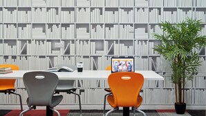 A conference room with a white table, two chairs, a laptop, a coffee cup, and a potted plant.
