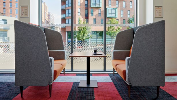 A modern room with two grey armchairs, a small table, and a view of a cityscape through large windows.