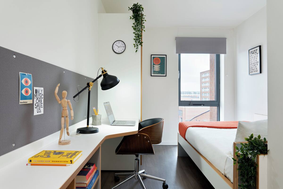 Quarto moderno com escrivaninha, um laptop, cama e janela com vista para a cidade.