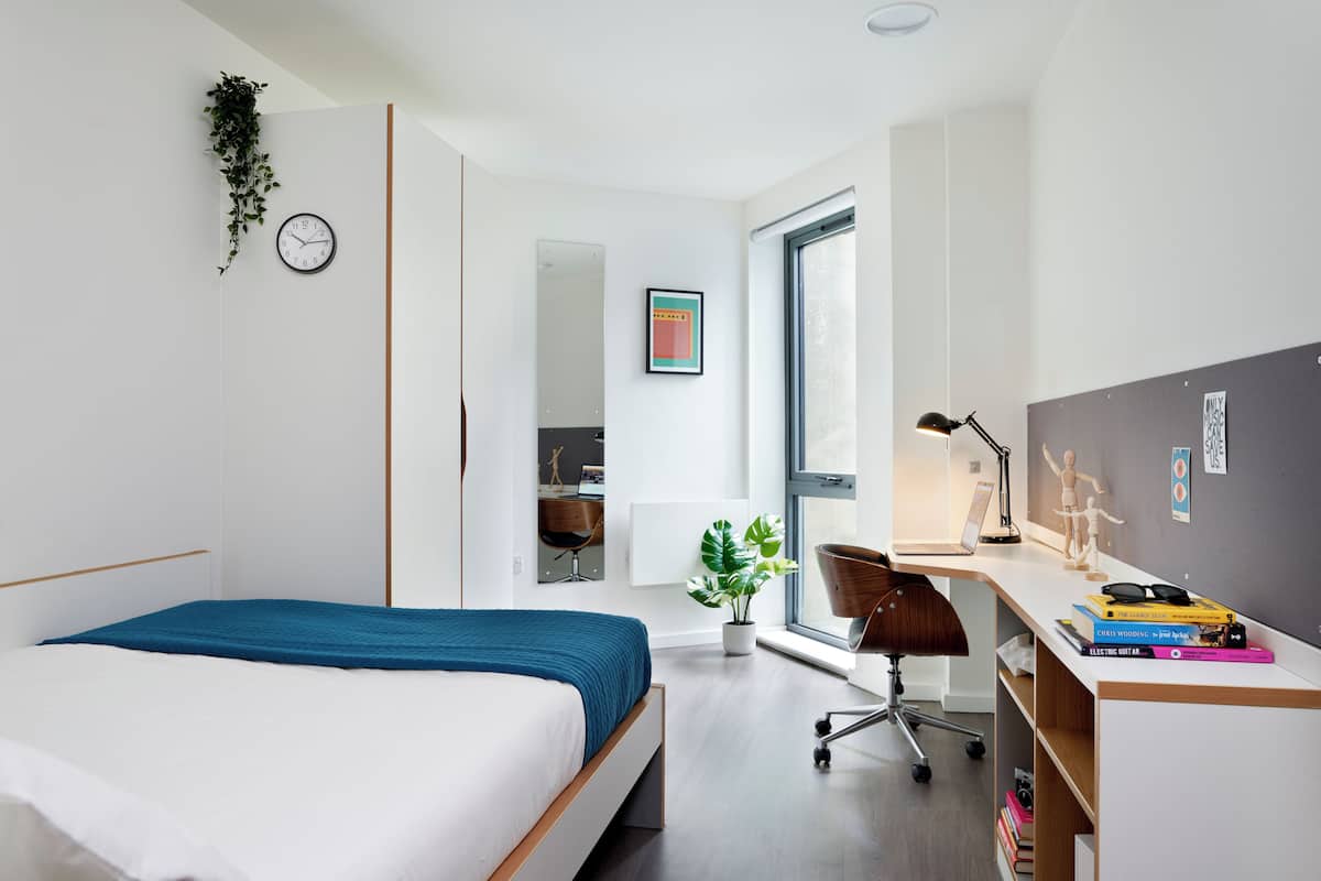 Quarto moderno com cama, escrivaninha, cadeira, janela e espelho.