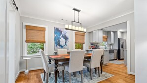 Un coin repas comprenant une table en bois, quatre chaises, un lustre et un grand tableau abstrait accroché au mur.