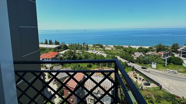 A balcony with a view of a coastal town, including a road, buildings, and the sea. - Aparthotel Greenhouse (Batumi)