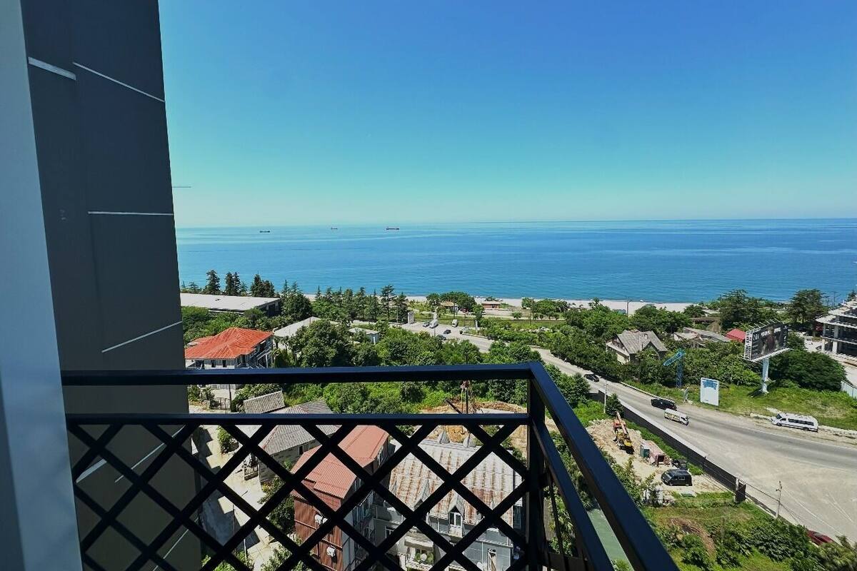 A balcony with a view of a coastal town, including a road, buildings, and the sea.