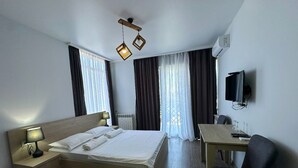 Ein Hotelzimmer mit Bett, Nachttisch mit Lampe, Schreibtisch mit Stuhl und Fernseher an der Wand.