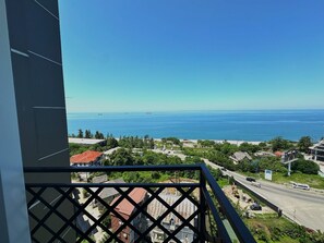 A balcony with a view of a coastal town, including a road, buildings, and the sea. - Aparthotel Greenhouse (Batumi)
