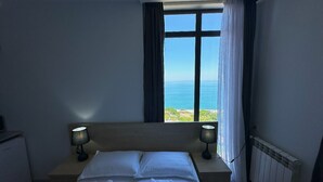 A hotel room with a large bed, two bedside lamps, a view of the sea, and a radiator. - Aparthotel Greenhouse (Batumi)