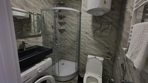 Ein modernes Badezimmer mit einer einachigen Duschkabine, einem Waschbecken mit schwarzer Ablagefläche, einer Toilette und einer Waschmaschine.